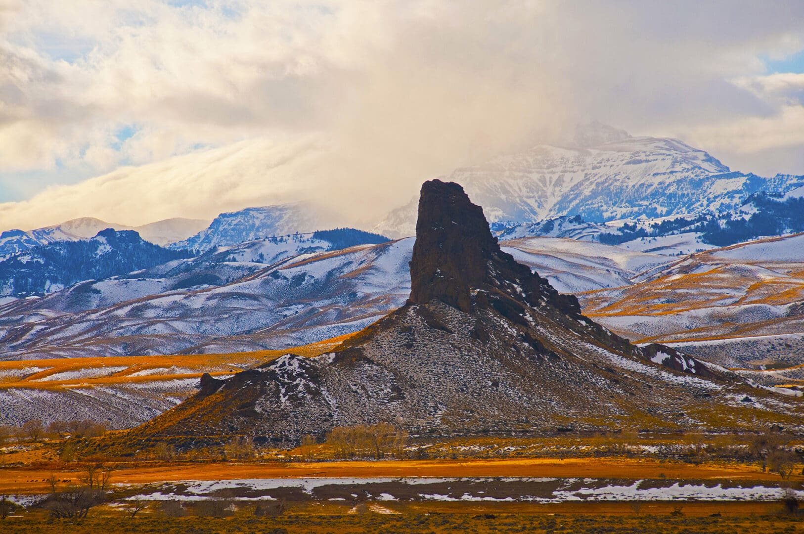 A rock formation in the middle of a field with snowy mountains in the background.