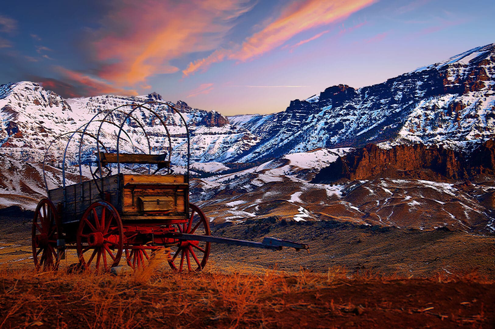 A wagon in the middle of a field with mountains in the background.